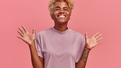 Mensch mit blonder Afro-Frisur streckt erfreut die Arme zur Seite