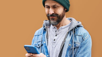 Mensch mit Mütze und Bart hält ein Handy in der Hand und lächelt