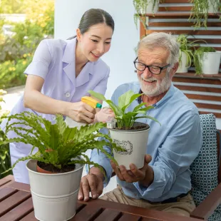 Ältere Person unterstützt eine Pflegekraft beim Blumengießen