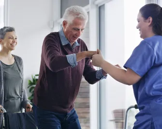 Ältere Person wird durch Pflegekraft beim Aufstehen unterstützt