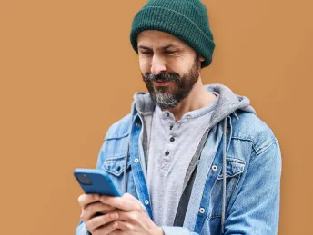 Mensch mit Mütze und Bart hält ein Handy in der Hand und lächelt