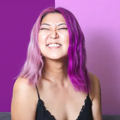 Person mit violetten Haaren lächelt mit geschlossenen Augen in Kamera