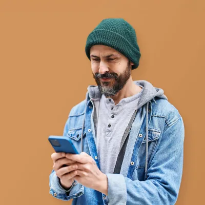 Mensch mit Mütze und Bart hält ein Handy in der Hand und lächelt