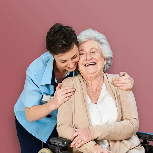 Pflegende Person umarmt eine sitzende ältere Frau